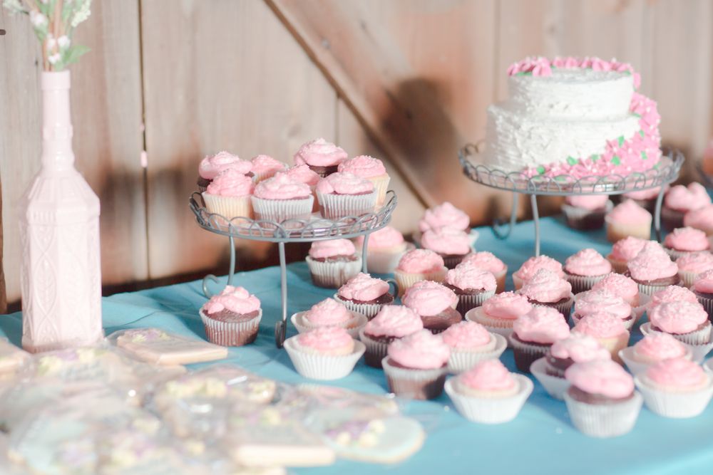 An elegant dessert table with pink cupcakes and a white wedding cake on tiered stands.