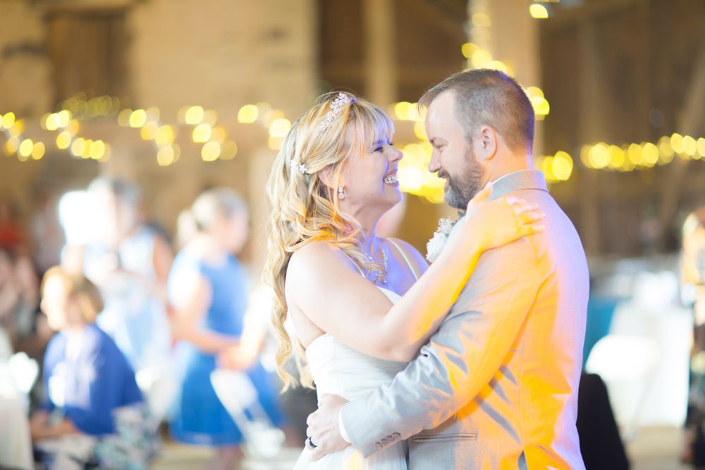 A couple dances intimately together under warm glowing lights at their wedding celebration.