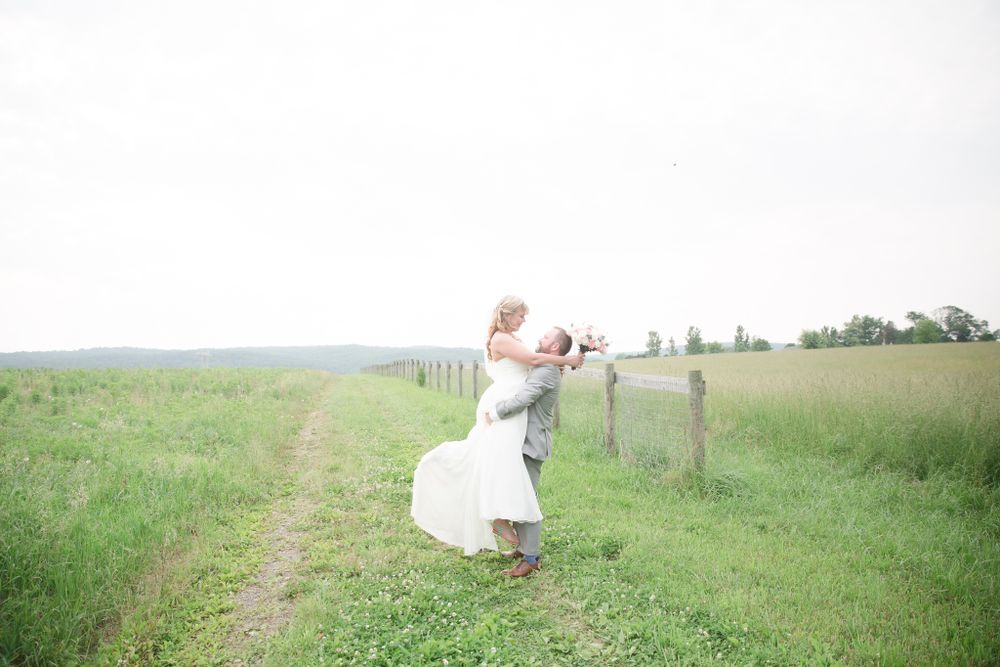 A couple dances playfully in a serene meadow on their wedding day.