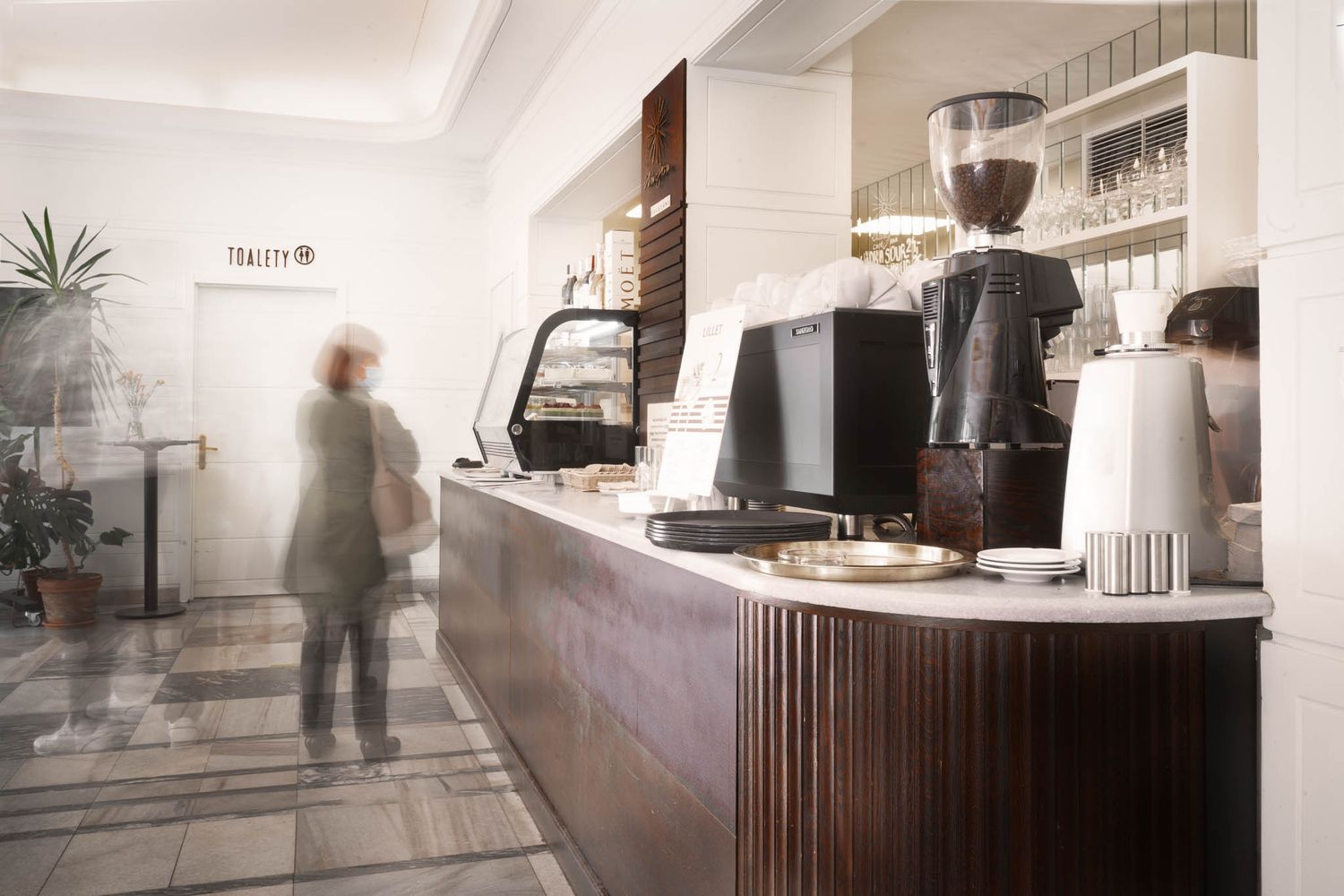 Blurry figure walking past modern coffee bar counter with equipment.