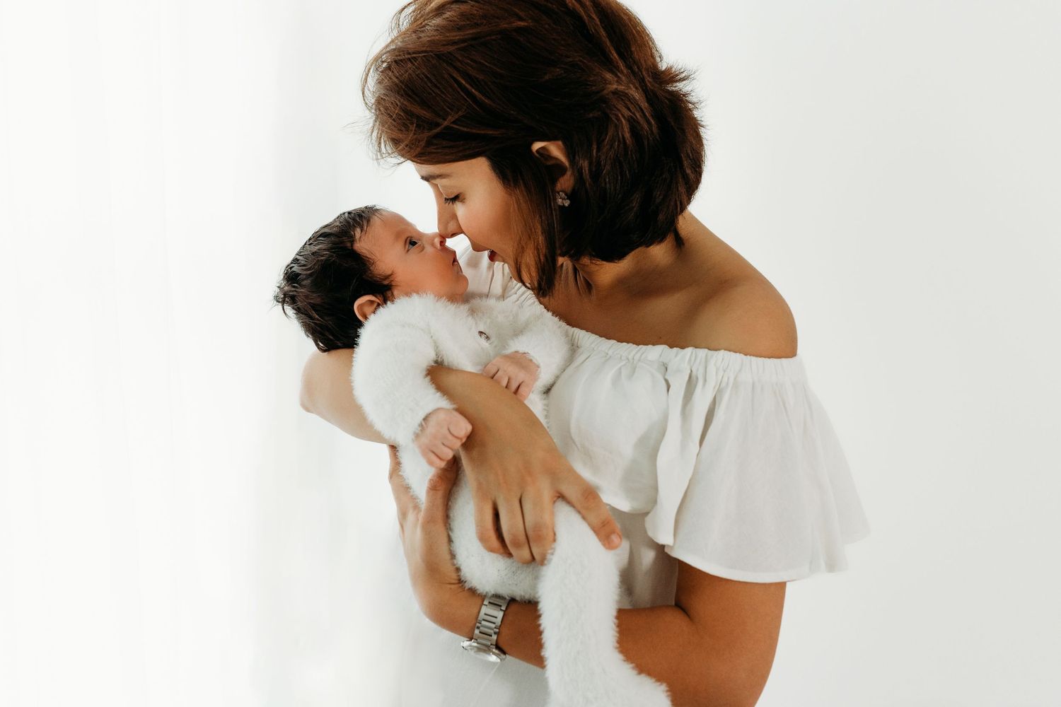 A tender moment captured in white as a newborn baby is cradled and kissed against a minimalist backdrop.