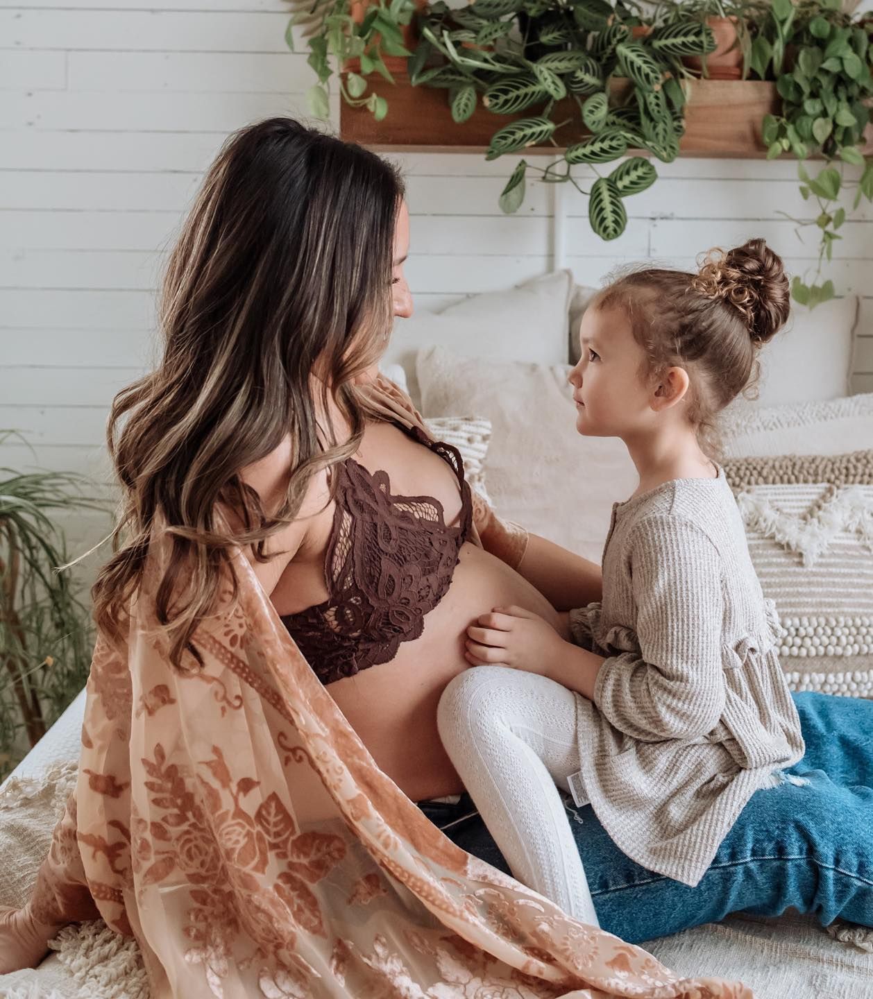 An intimate maternity photo showing a touching moment between mother and child surrounded by indoor plants.