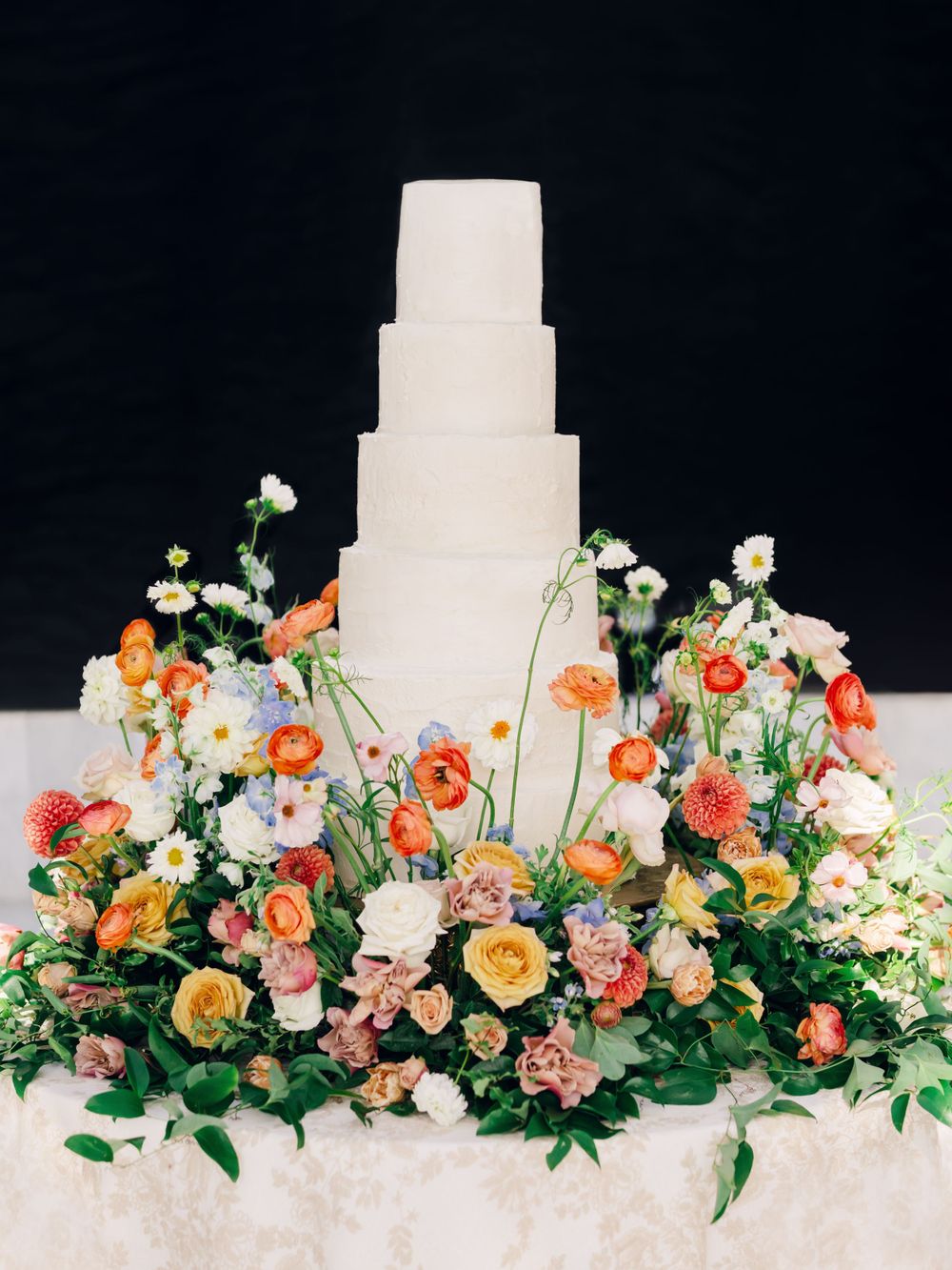 White tiered wedding cake decorated with cascading coral and peach flowers.