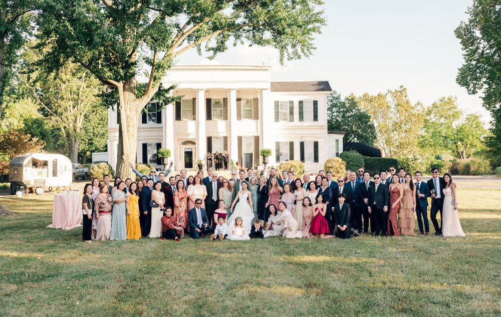 Large wedding party poses in front of white colonial mansion.