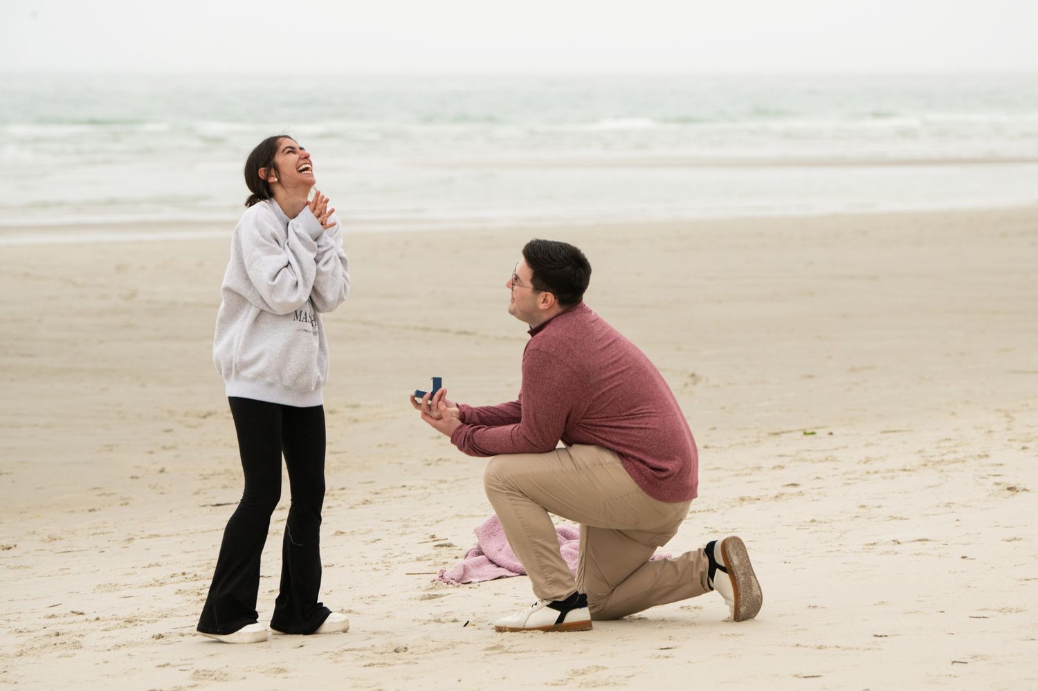 A couple shares a special moment on a sandy beach during a proposal.