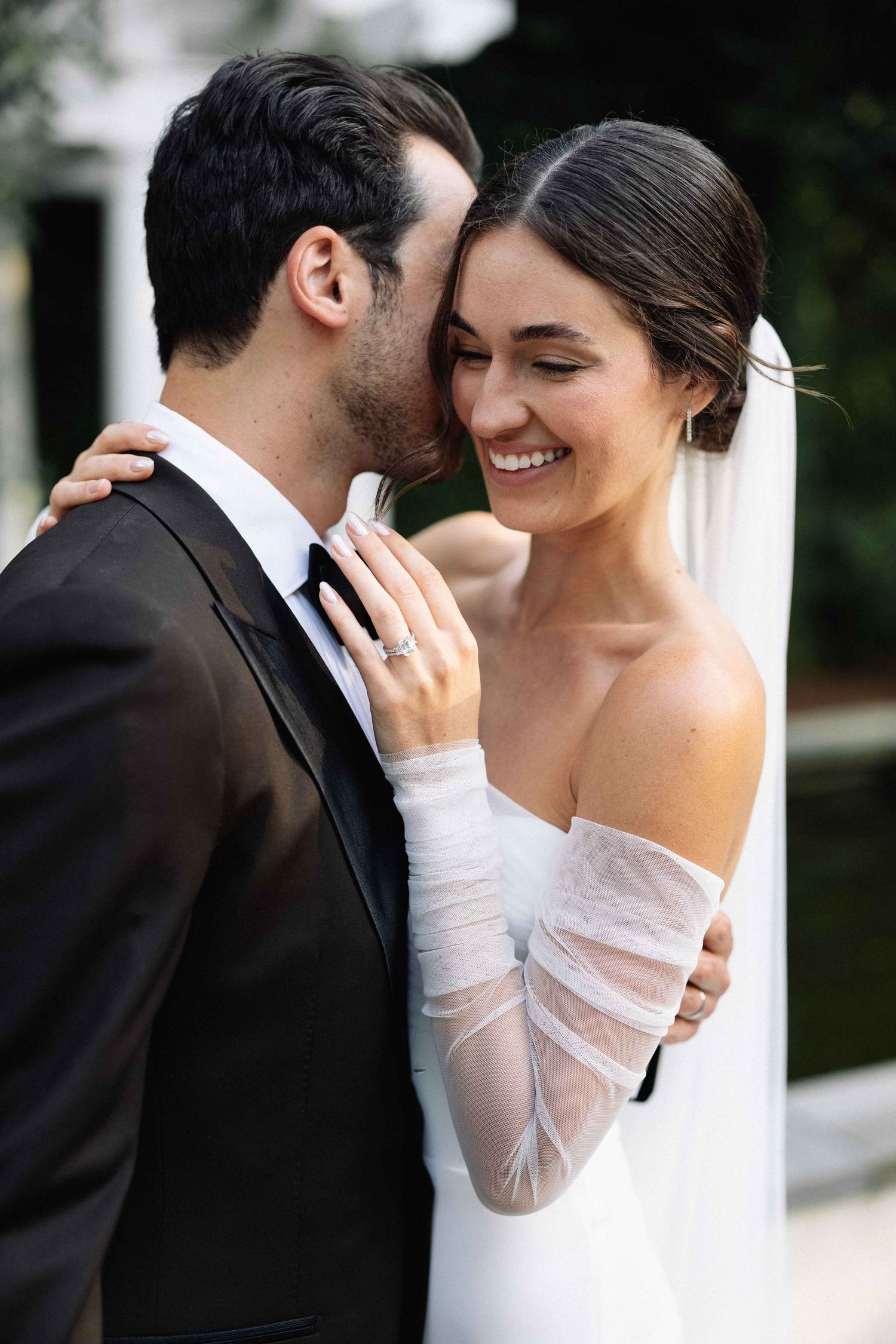 An elegant bride, smiling on her wedding day while holding onto her husband at The William Aiken House in Charleston, SC