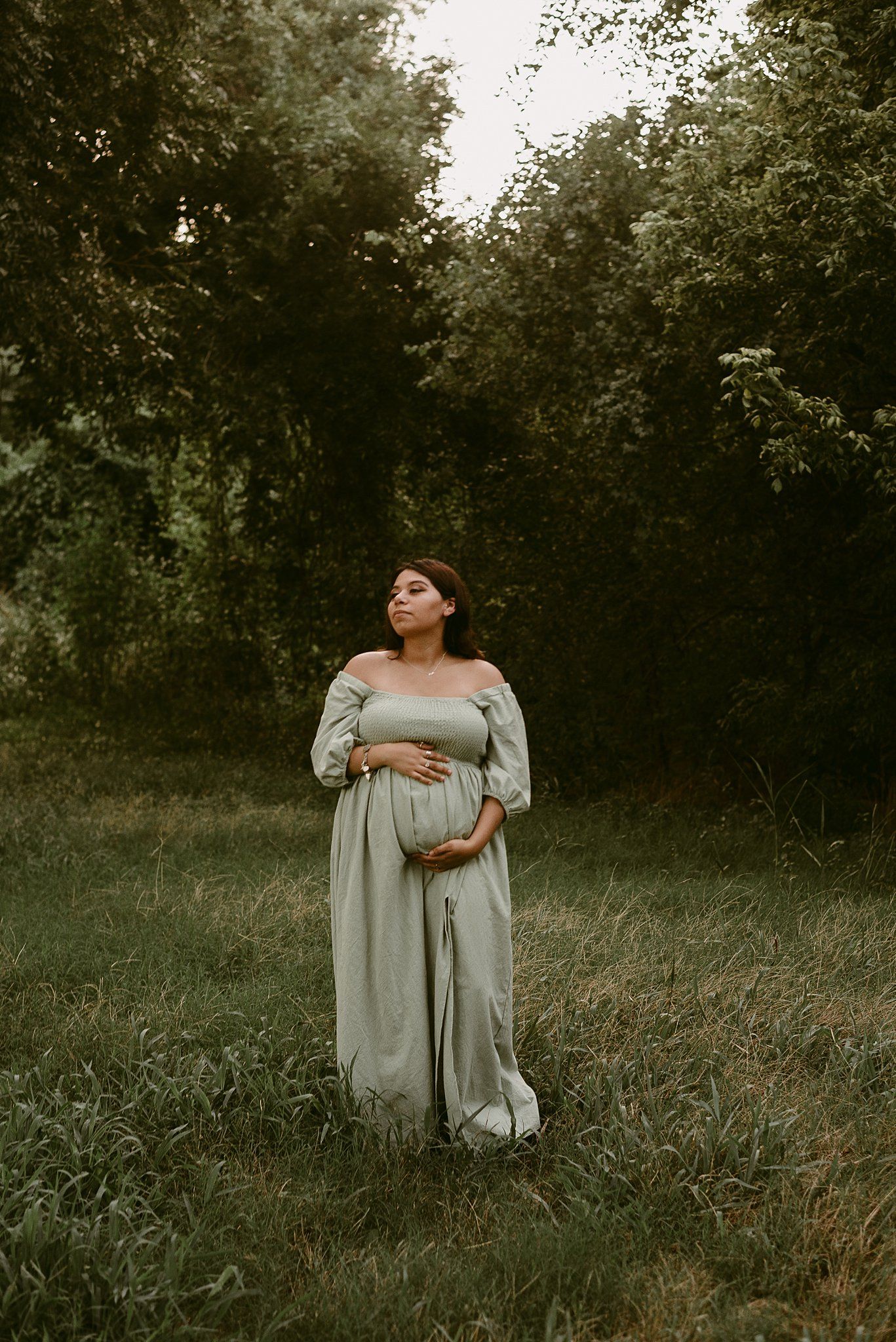 Maternity portrait against lush forest backdrop in dreamy lighting.
