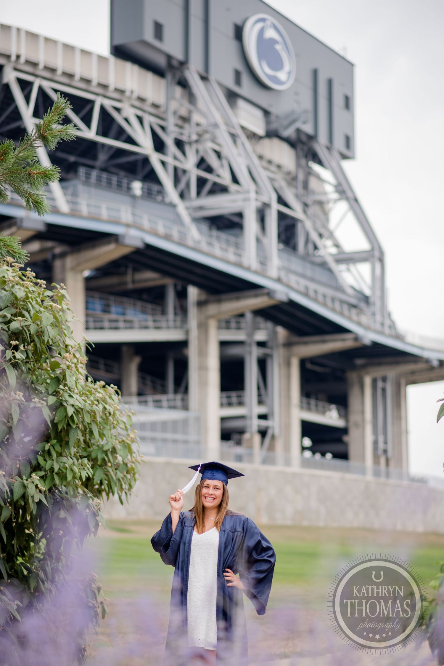 A graduate in academic regalia poses in front of Penn State's Beaver Stadium architecture.