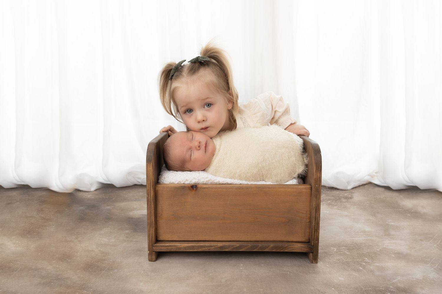 Small child peeking over wooden crate filled with cream colored cushioning.