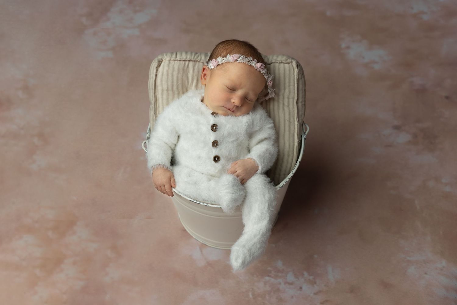 Baby in white outfit posed in vintage-style chair against textured backdrop.