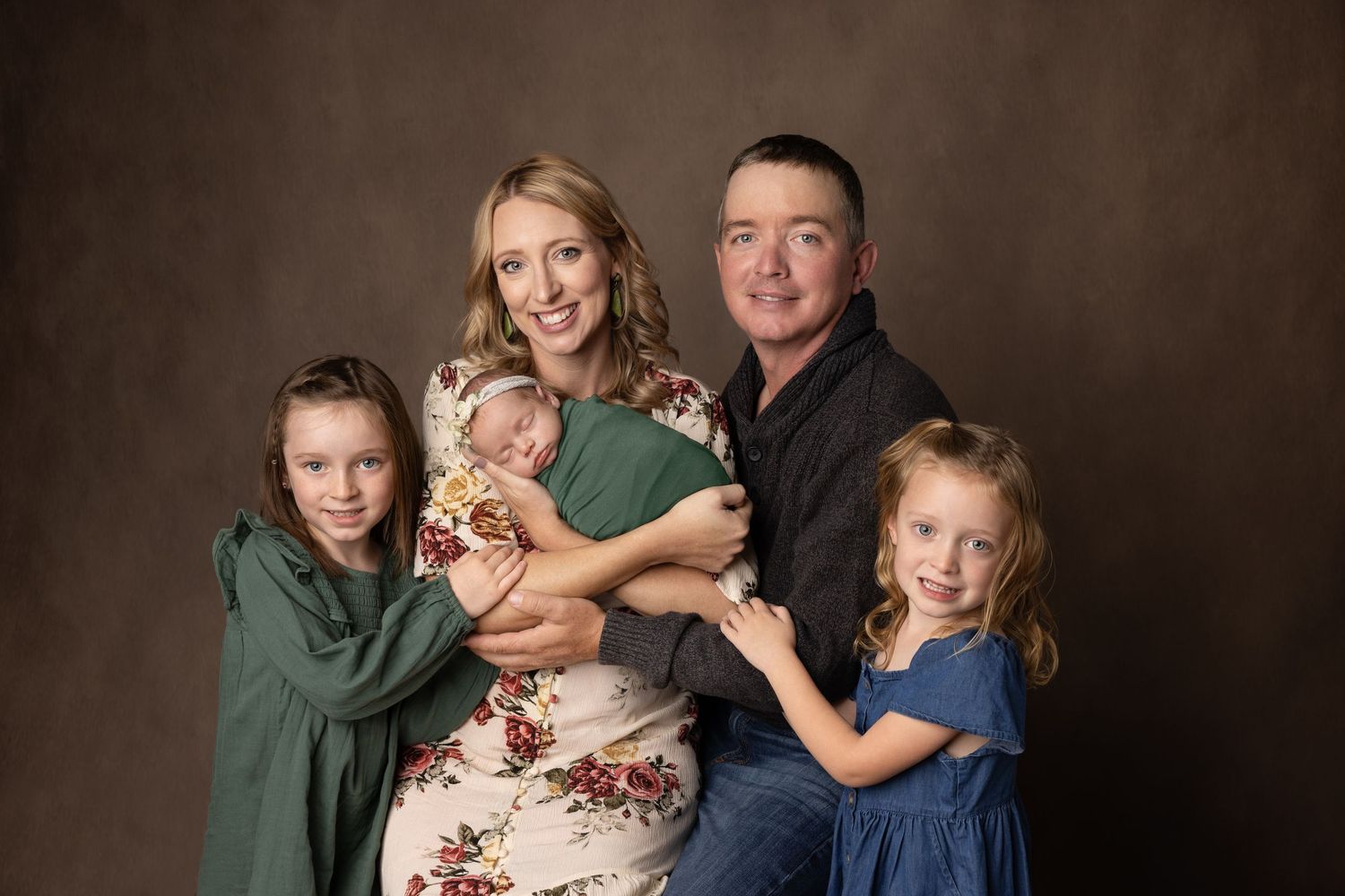 Studio portrait of family group in coordinated green and floral outfits against brown backdrop.