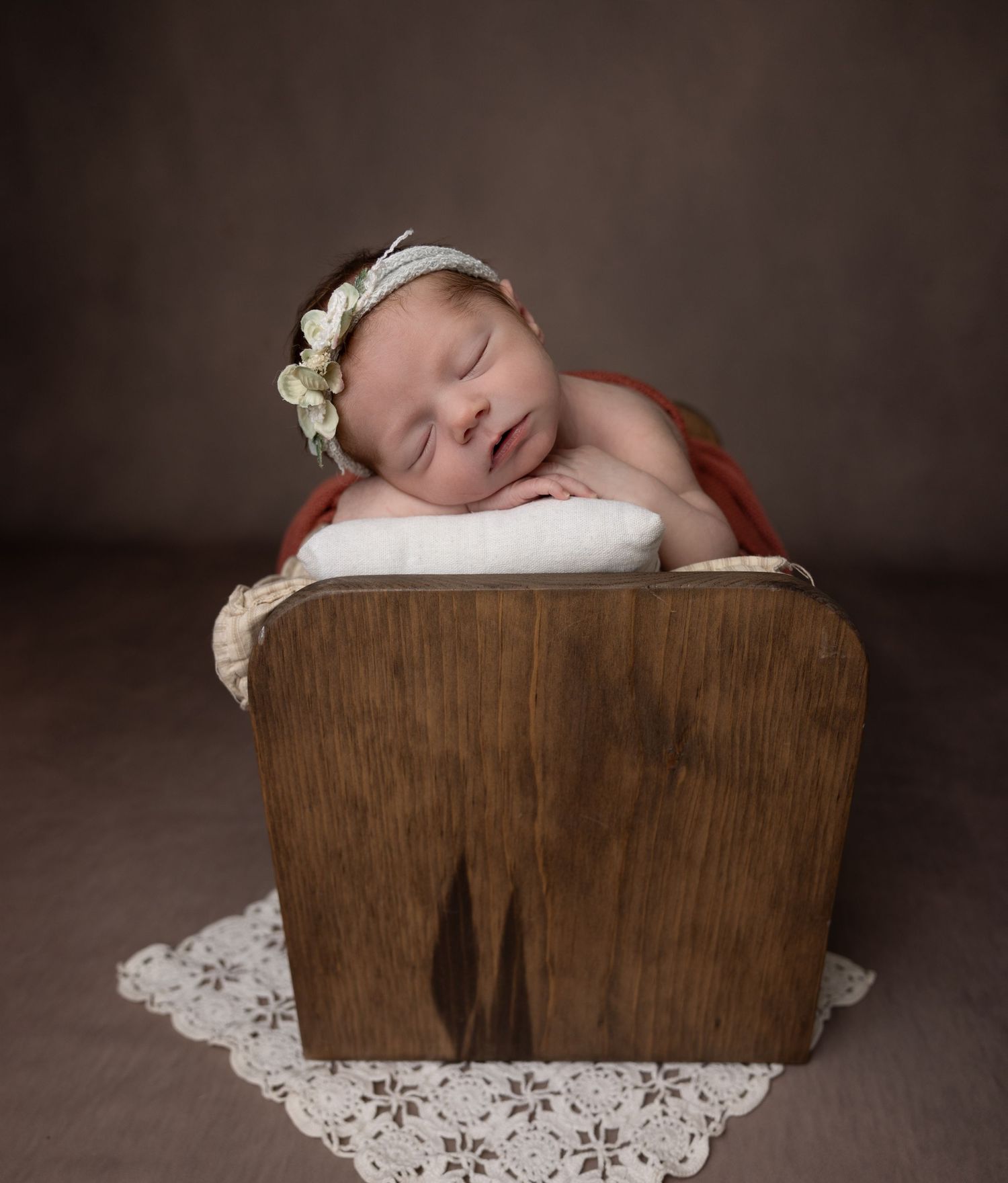 Sleeping baby in rustic wooden crate with lace doily and floral headpiece.