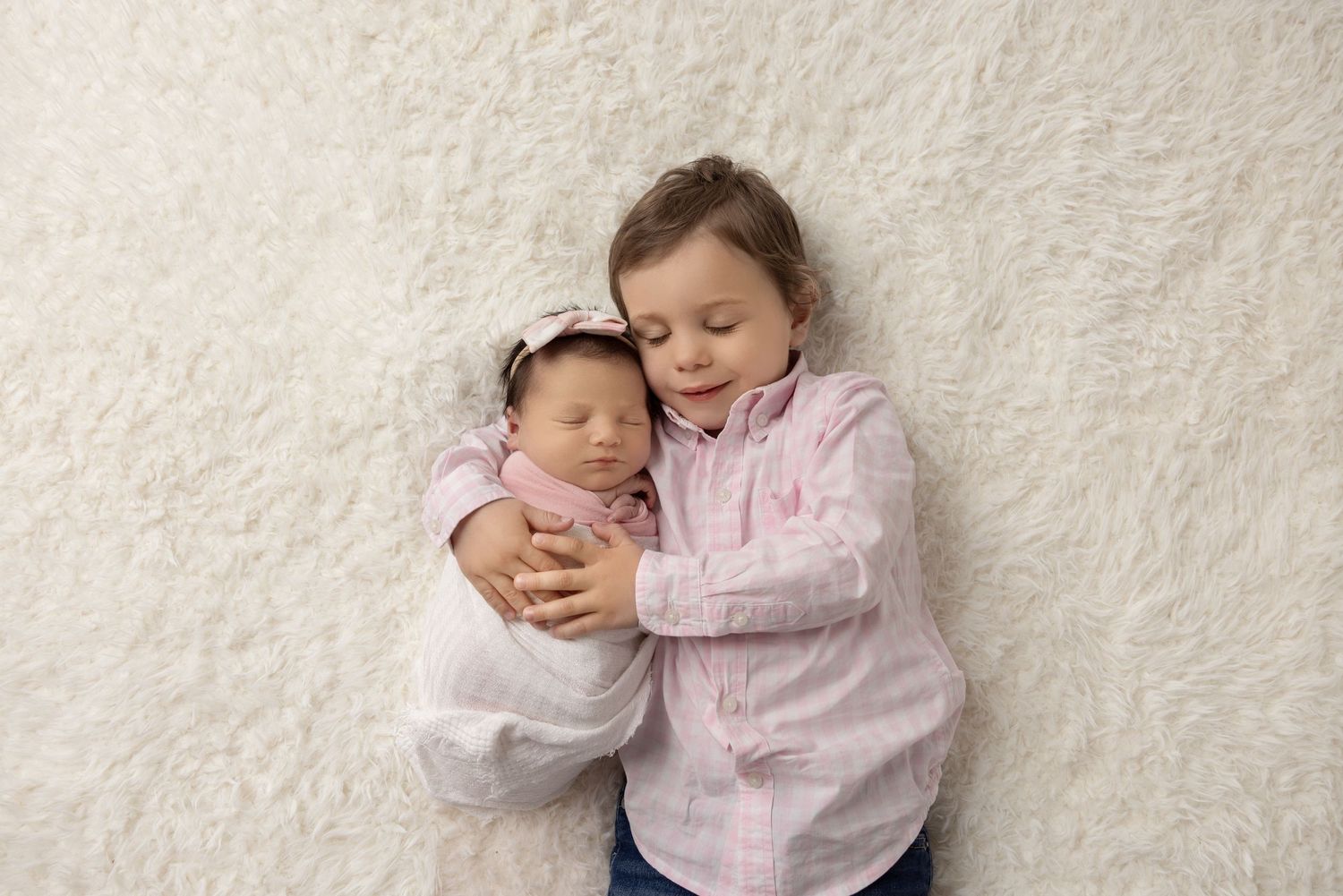 Baby resting peacefully in pink outfit against white textured background.