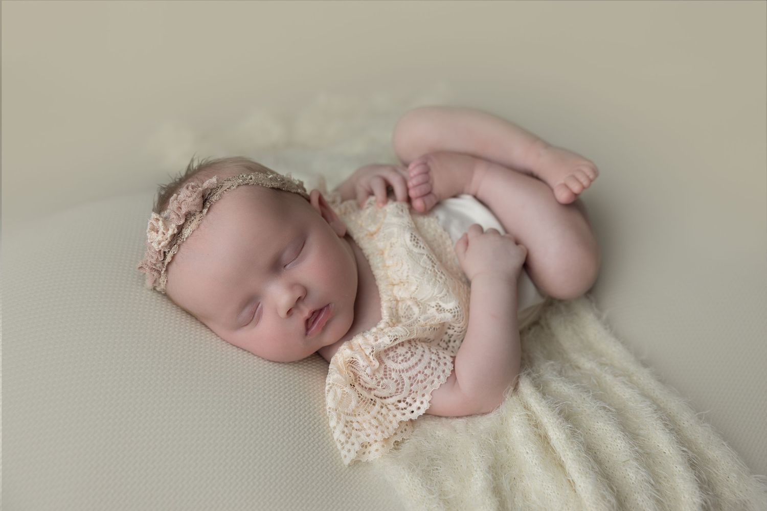 Newborn baby sleeping on cream colored fabric with delicate lace details.