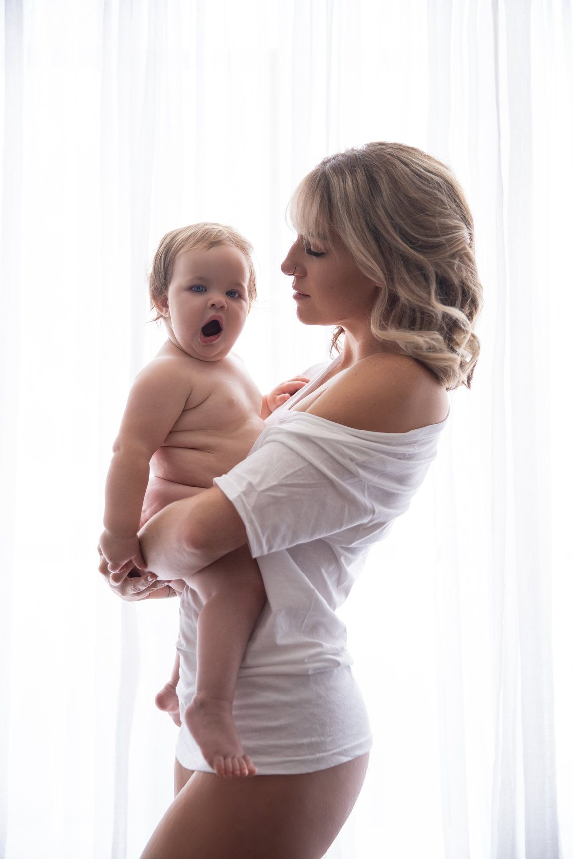 Mother and baby share tender moments in bright white portrait series.