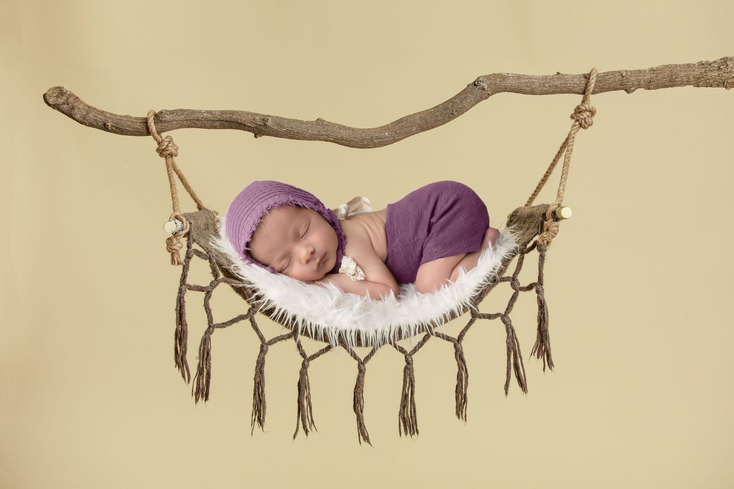 Small baby sleeping in rustic branch hammock with feather decorations.