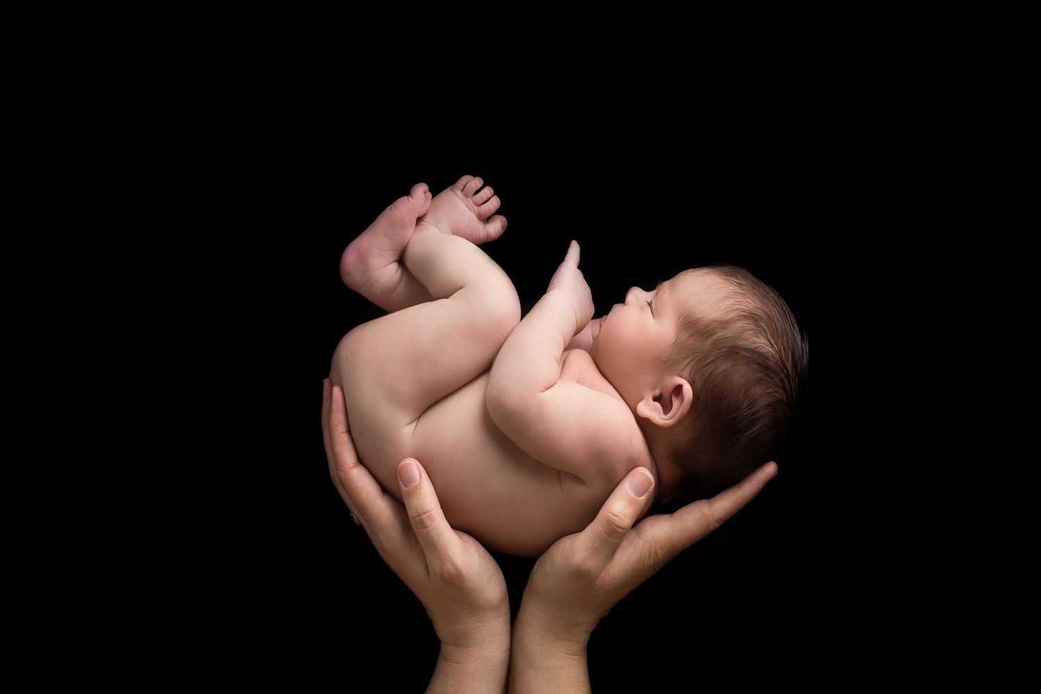 Artistic black and white portrait of infant's silhouette against dark background.