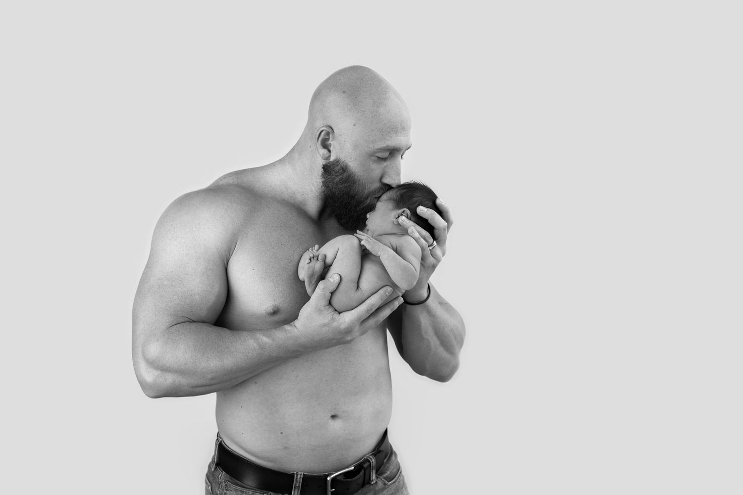 A shirtless muscular man leaning down to kiss his bicep muscles during a flexing pose.