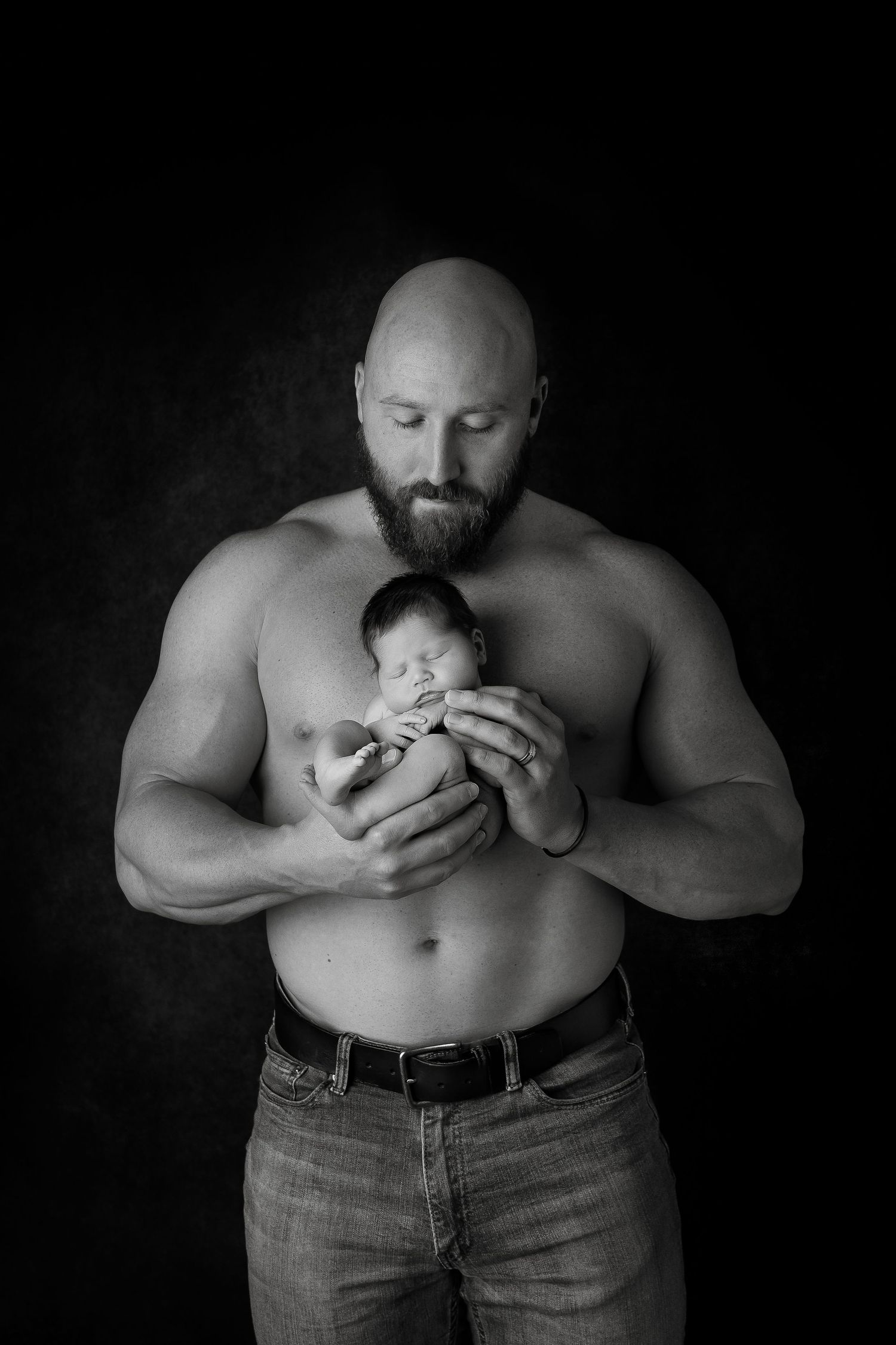 Intimate black and white portrait of parent and newborn against dark background.