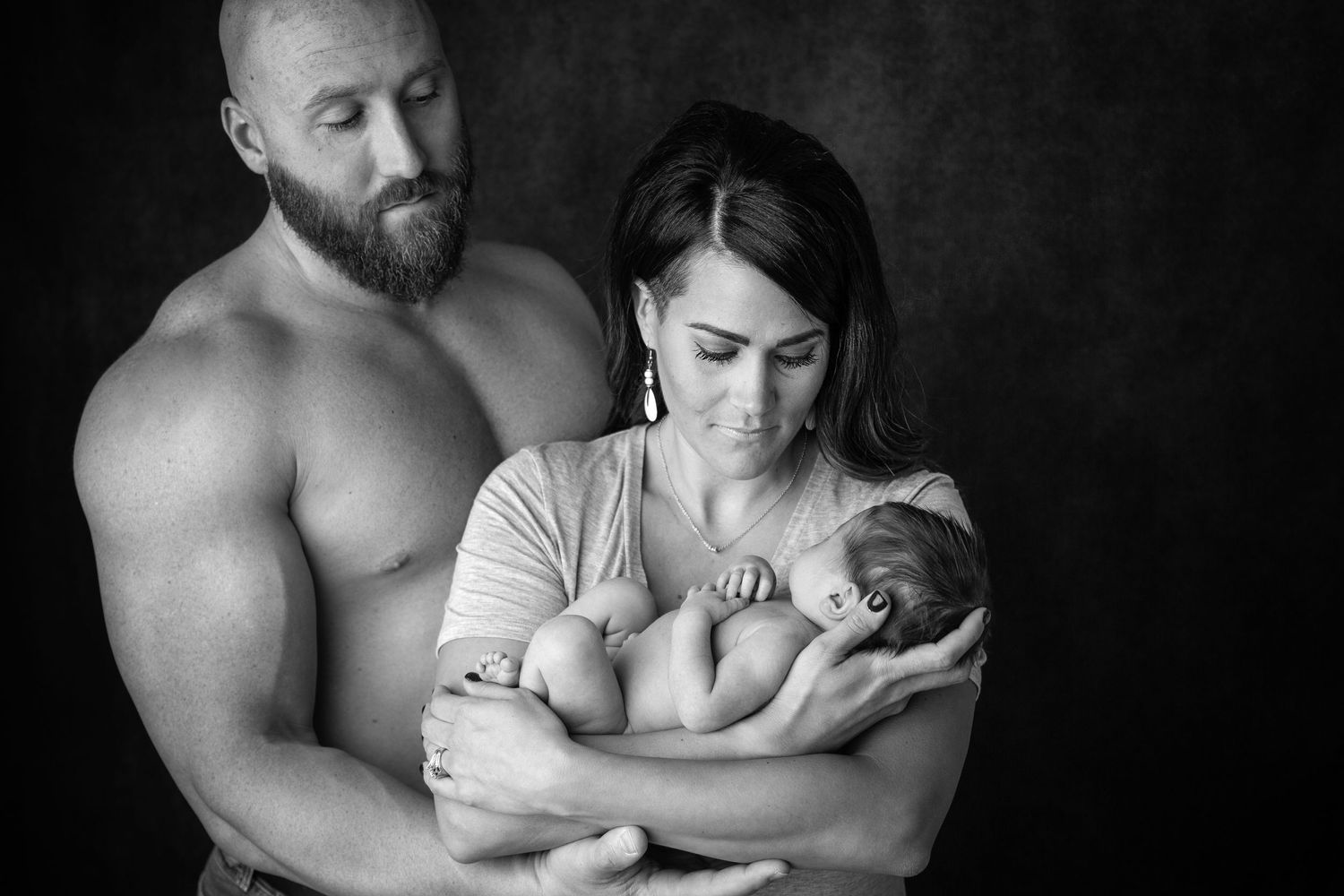 Intimate black and white family portrait showing tender moment with newborn baby.