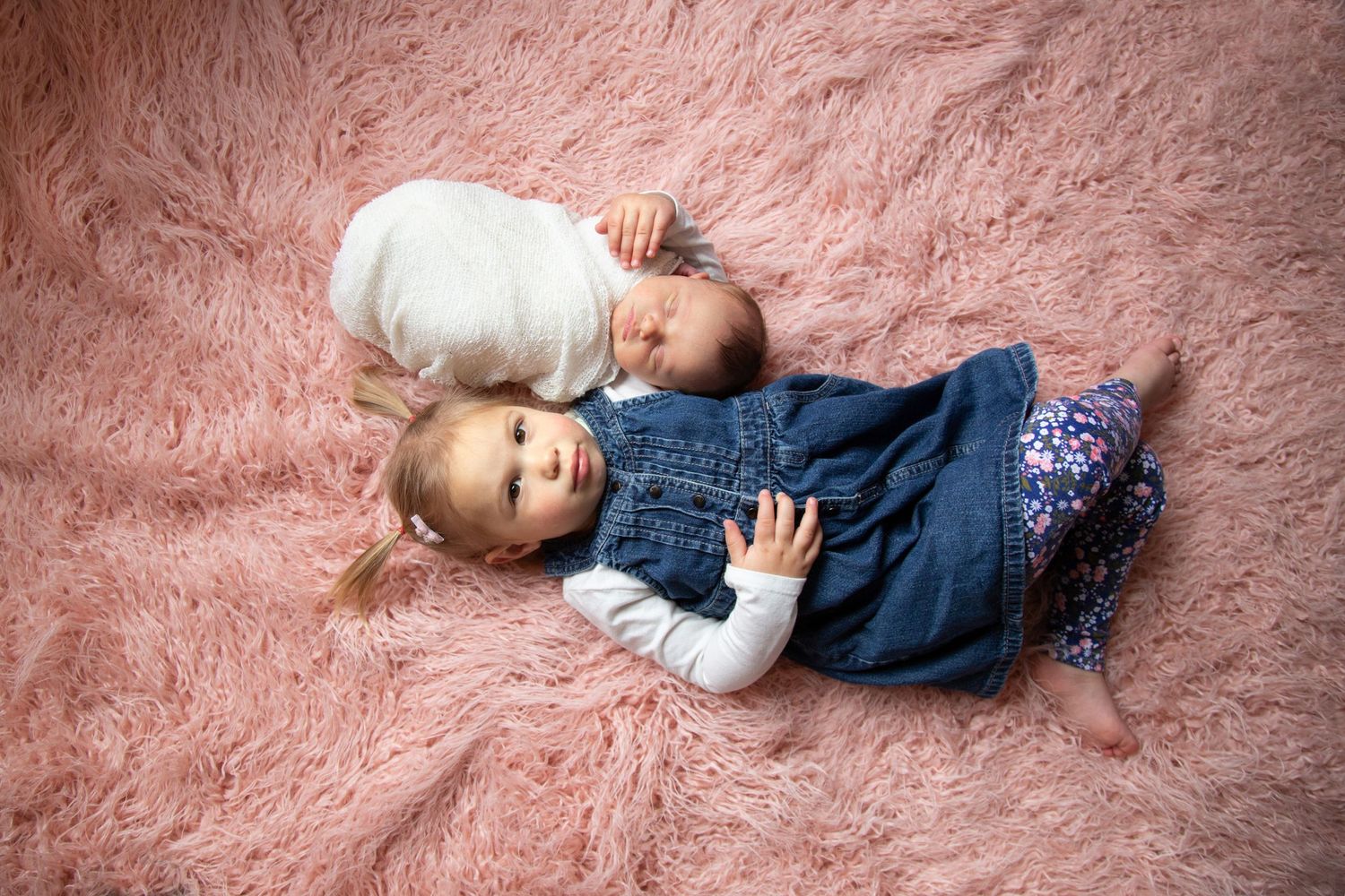 Two young children lying together on pink plush carpet during photo session.