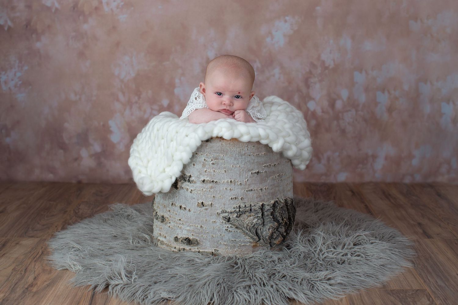 Professional newborn photo with baby on textured gray backdrop and delicate lace wrap.