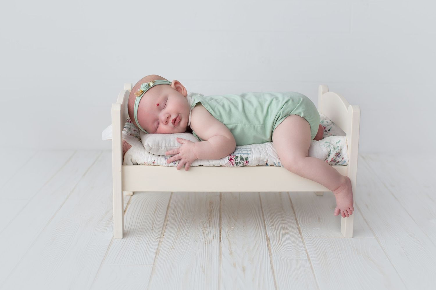 Peaceful sleeping baby in mint green outfit on simple white bed setting.
