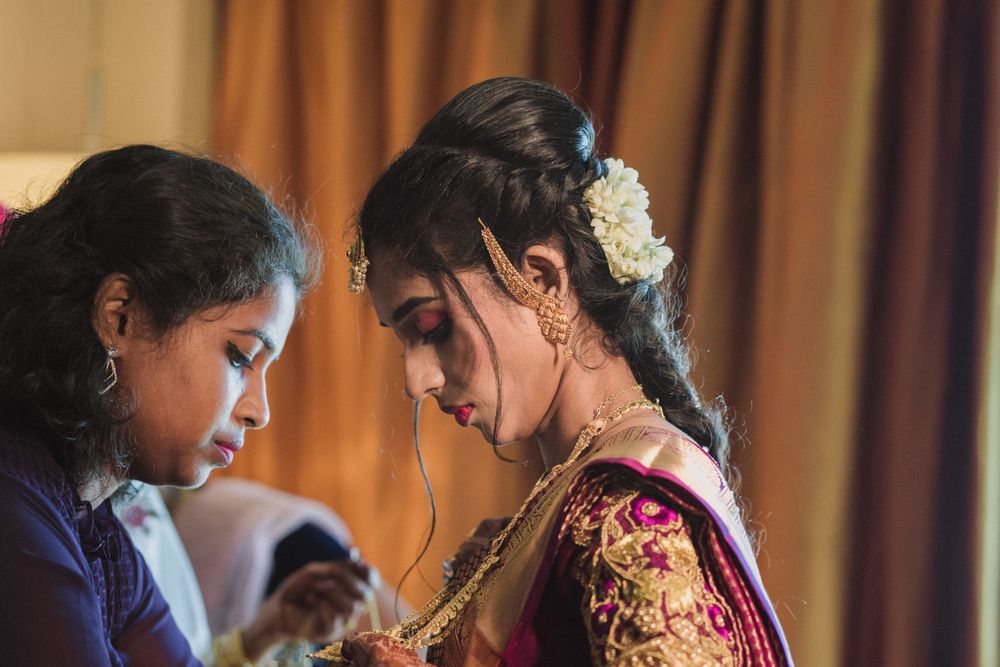 Traditional Indian bride wearing burgundy and gold lehenga gets final touches on her wedding day preparations.
