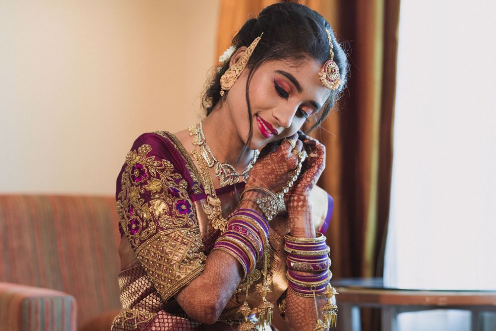 Bride in ornate burgundy and gold wedding attire adorned with jewelry speaks on phone during preparations.