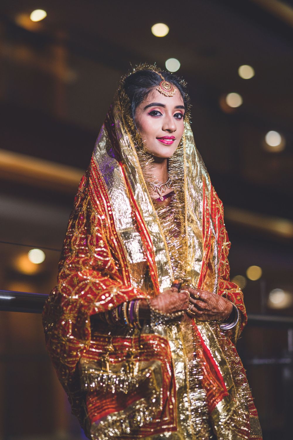 Bride adorned in sparkling red and gold wedding attire with traditional Indian jewelry and makeup.