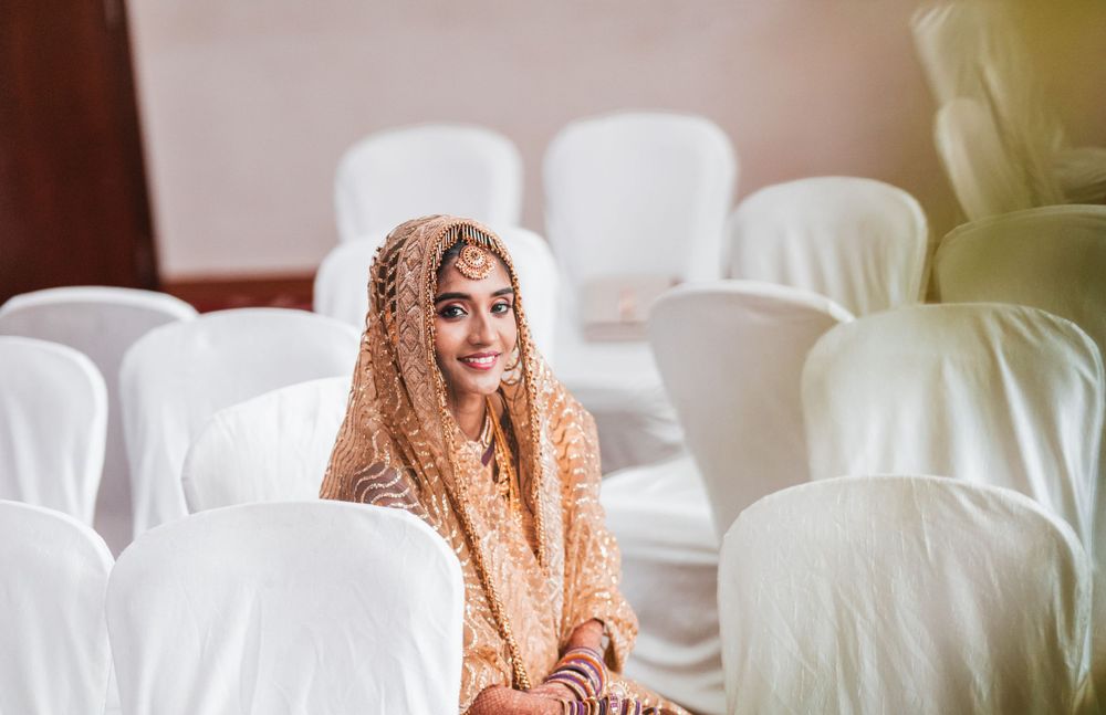 Someone wearing a peachy-orange embroidered veil sits among white chairs in an indoor setting.