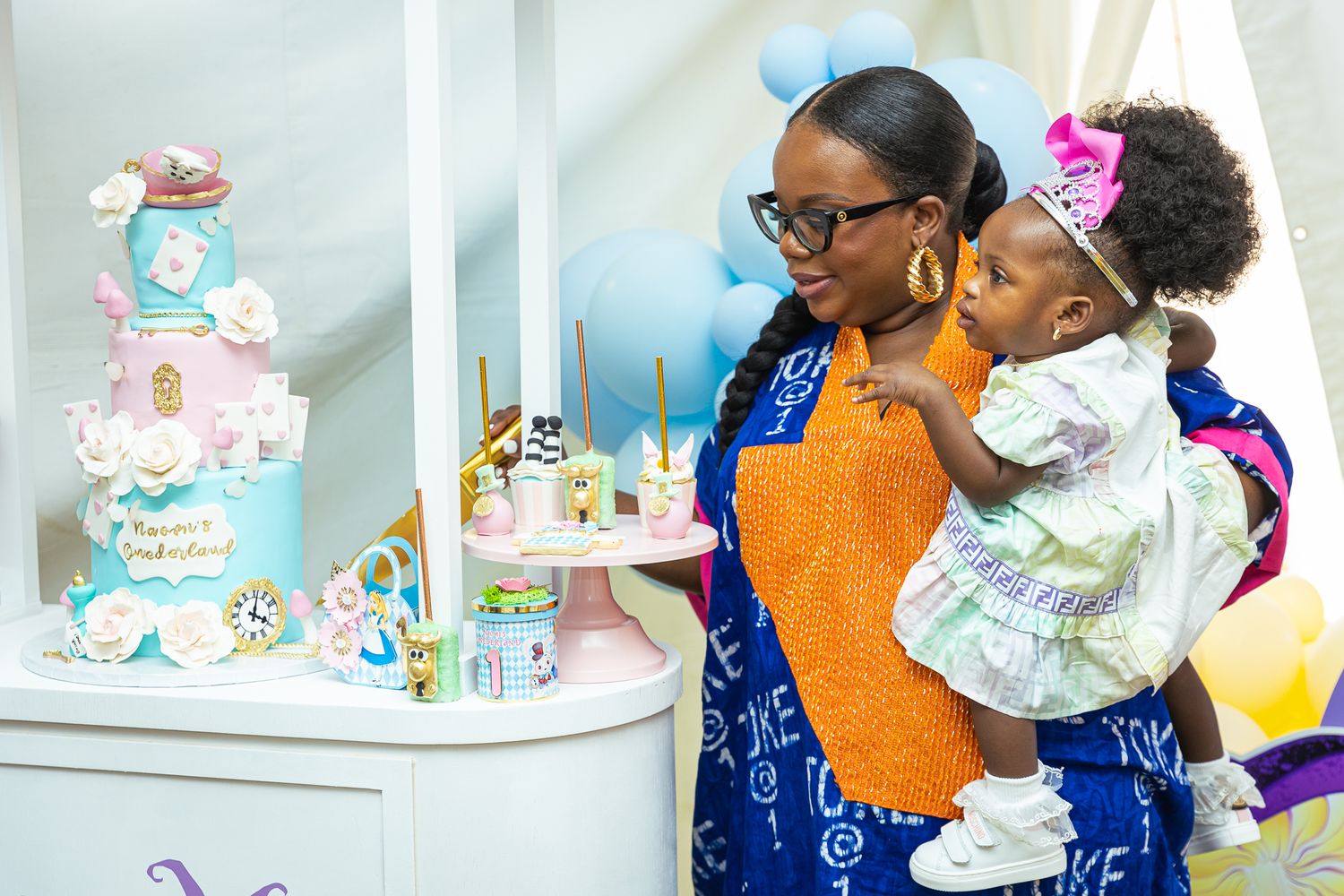 Woman holding child views decorative cakes at a festive celebration.