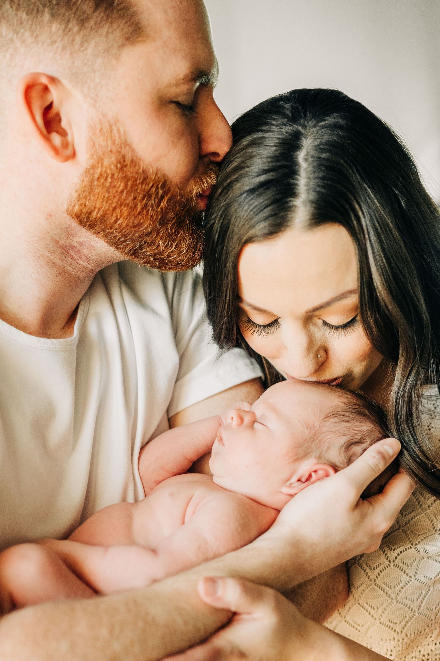 mom and dad kissing newborn during photo session in Frisco, TX