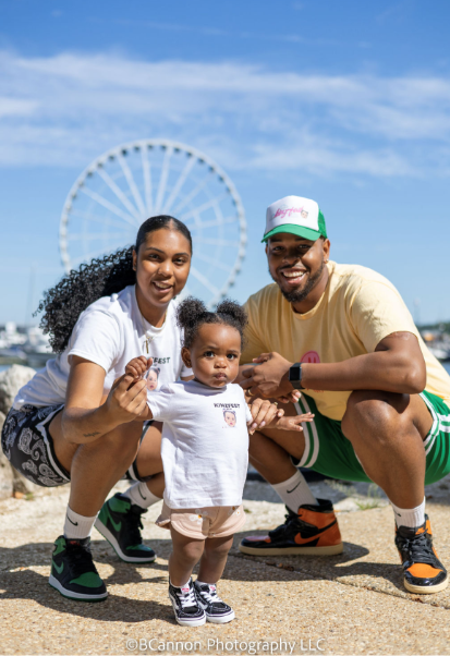 Family poses together near a ferris wheel at an outdoor amusement park.