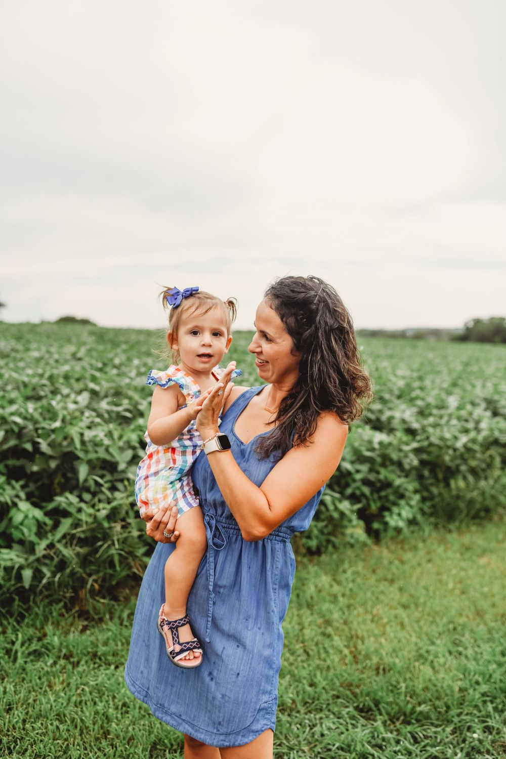 Mother and child sharing playful moment together in front of soybean field.