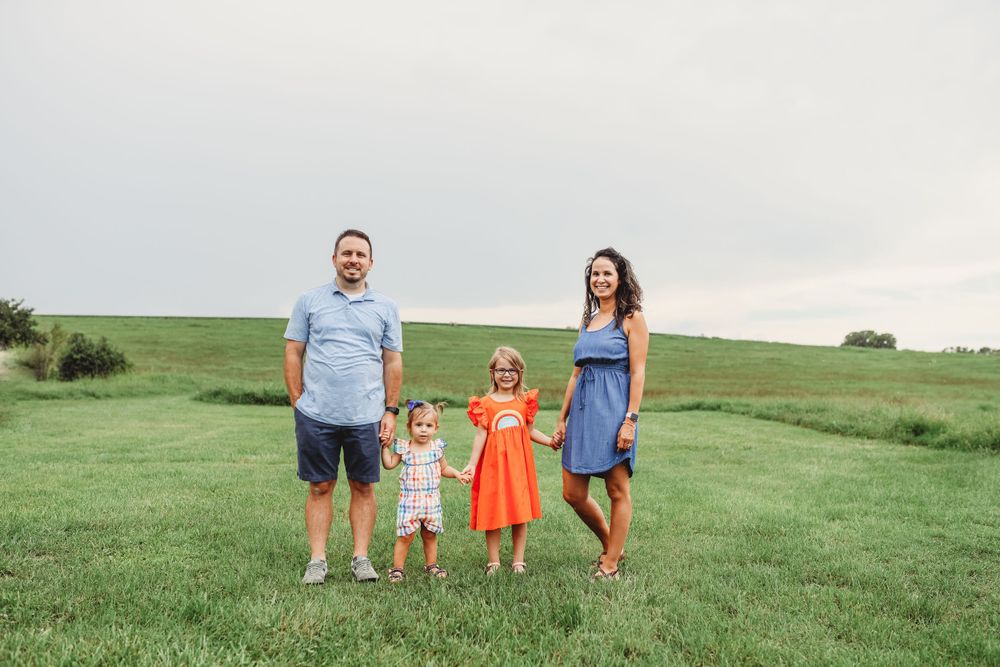 Family standing together in open green field under cloudy sky.