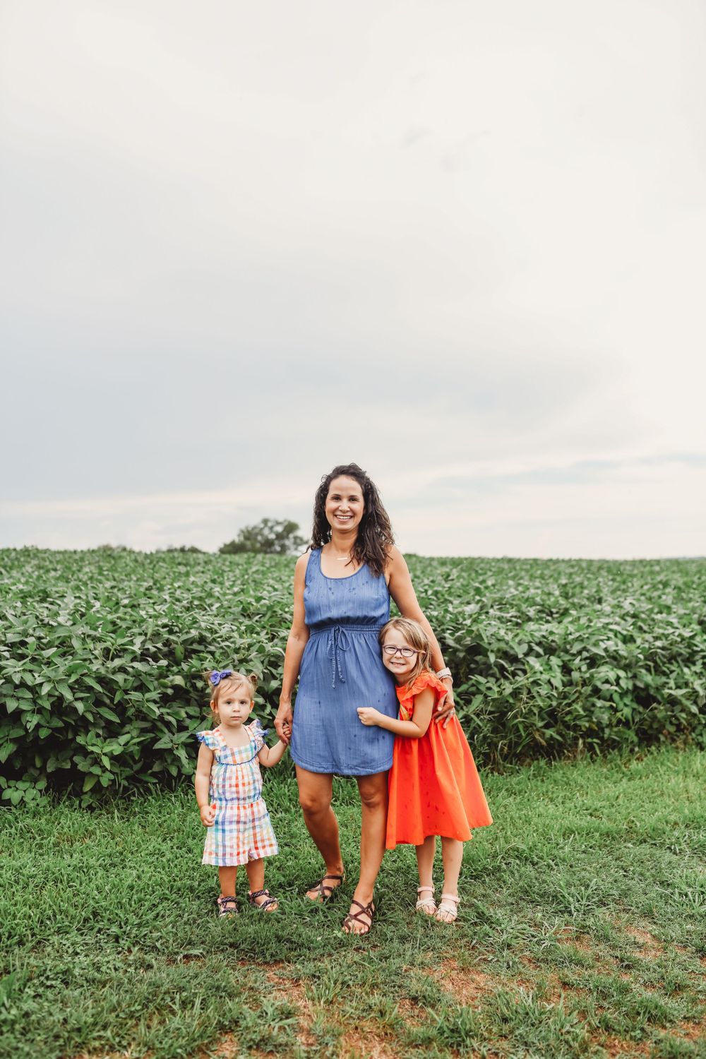 Family standing together at edge of soybean field on summer day.