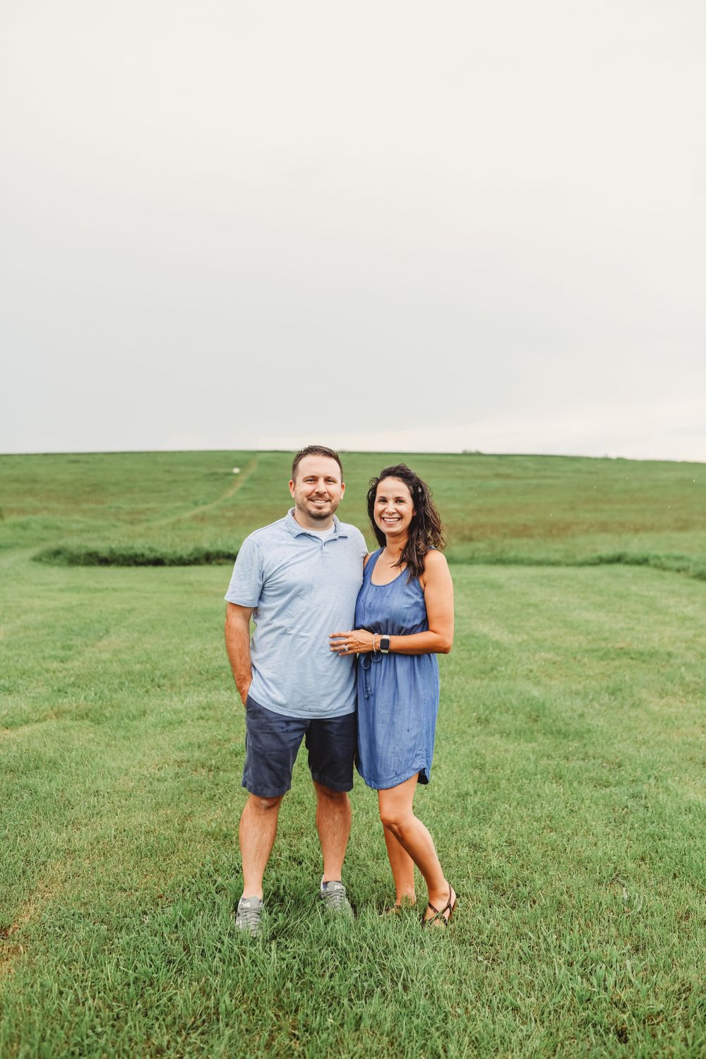 Couple posing together in casual attire on grassy hillside.