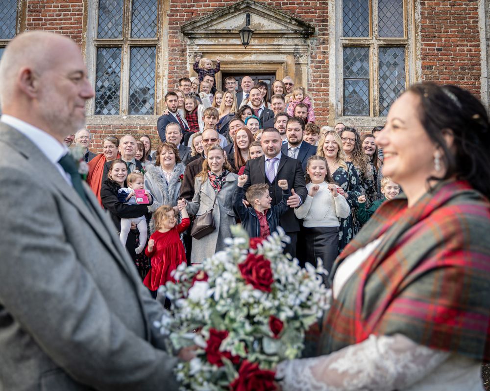 Wedding celebration outside historic brick building with gathered guests and floral arrangements.