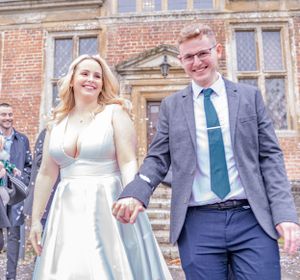 Wedding party walking and laughing together outside historic brick building.