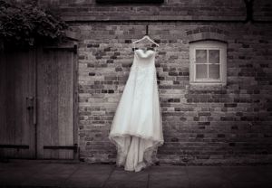 Wedding dress hanging against rustic brick walls in artistic black and white composition.