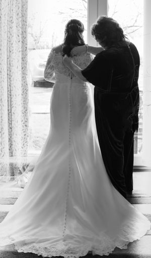 Silhouette of couple in wedding attire standing by window in black and white.