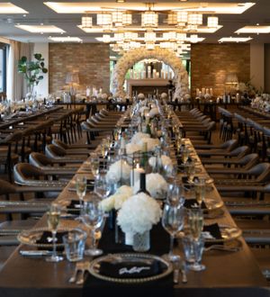 Long banquet tables set for a wedding reception with white centerpieces and modern lighting.
