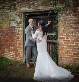 Wedding couple poses against rustic brick wall with climbing ivy.