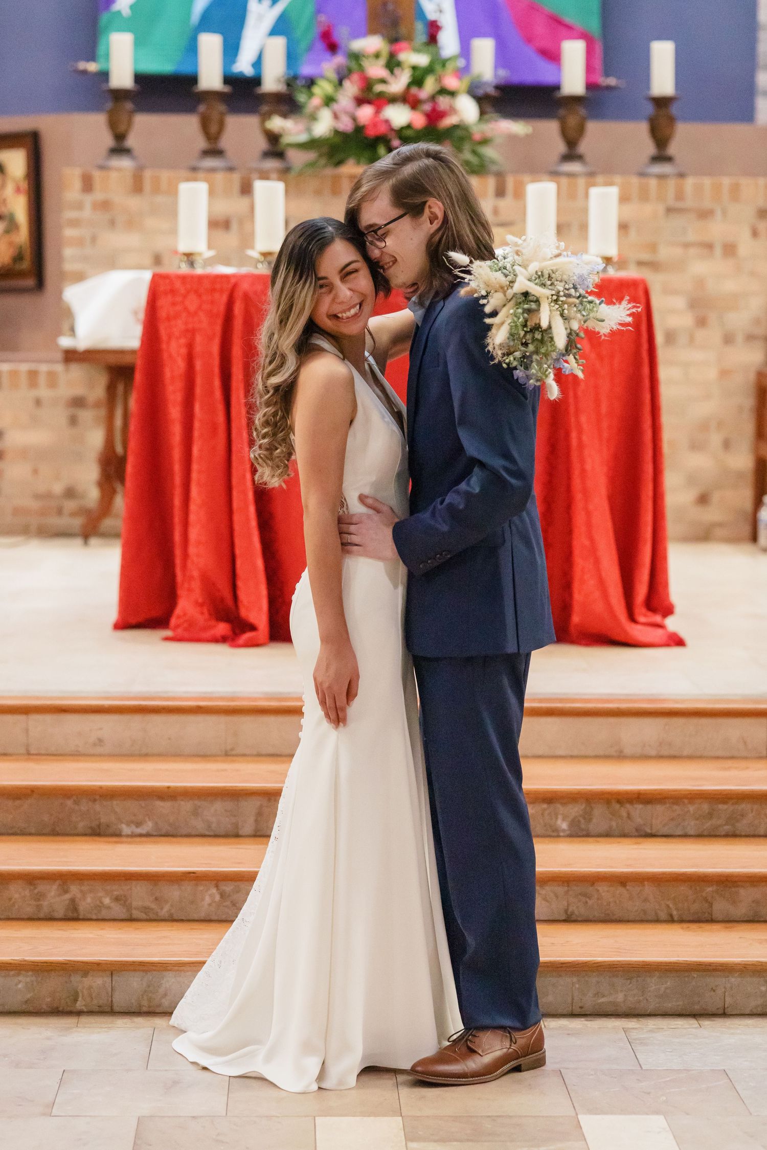 Wedding couple shares romantic moment at church altar with red decor and colorful backdrop.
