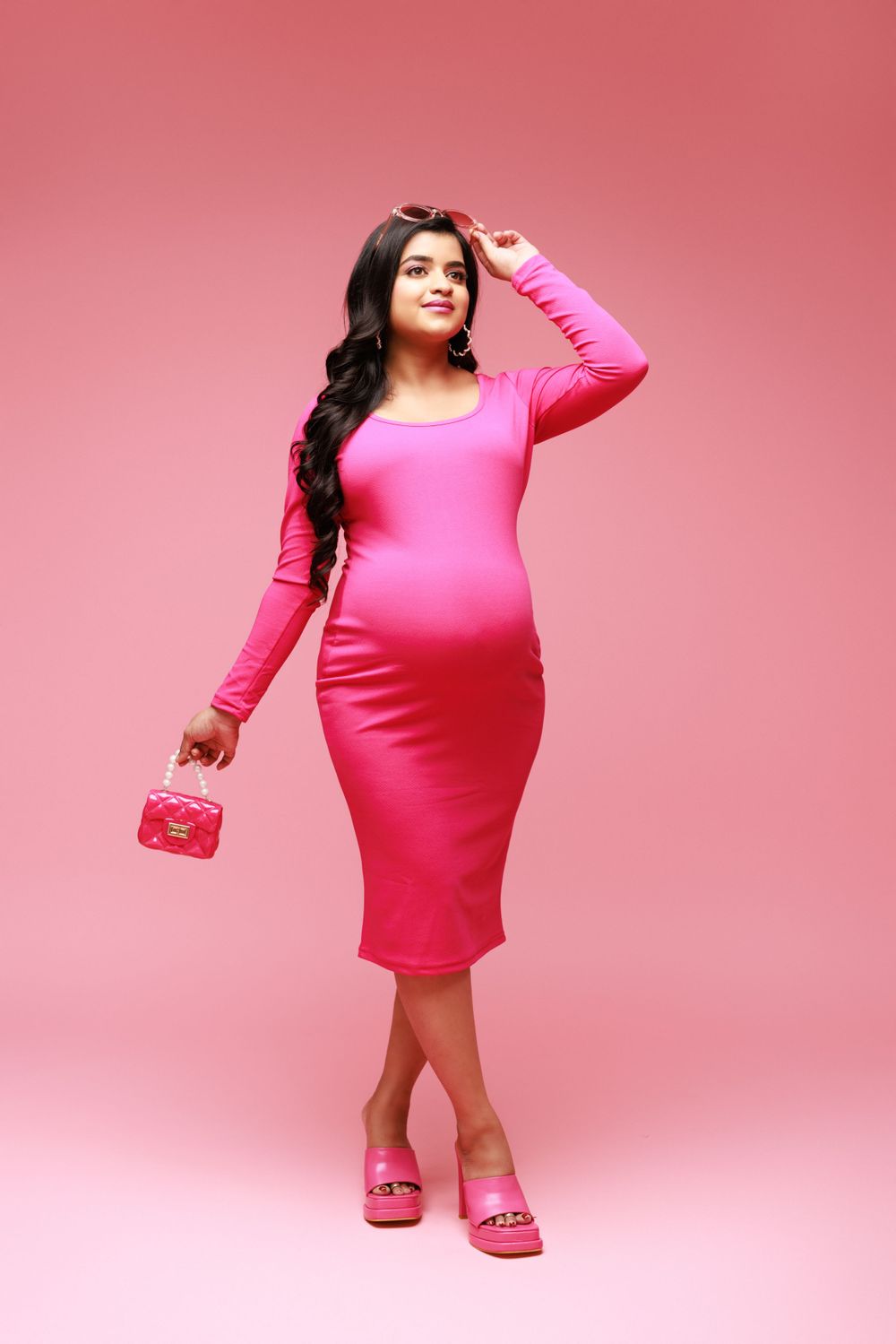 Fashion-forward maternity portrait in hot pink dress with matching accessories against pink background.