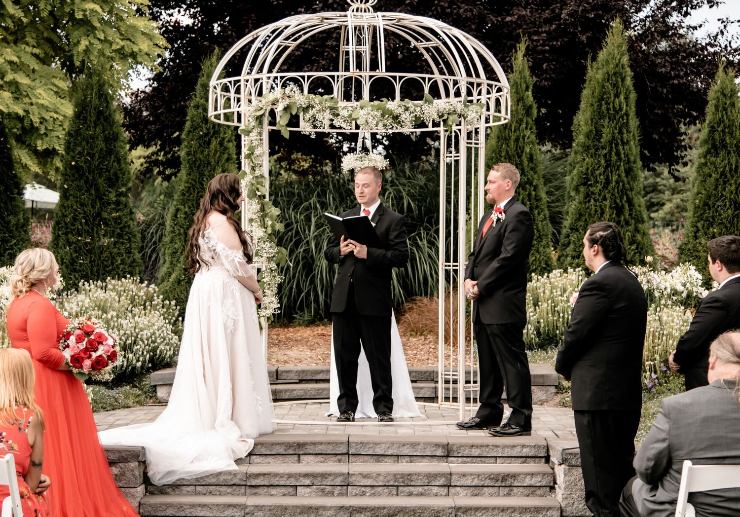 Wedding ceremony under white gazebo with guests seated on either side.
