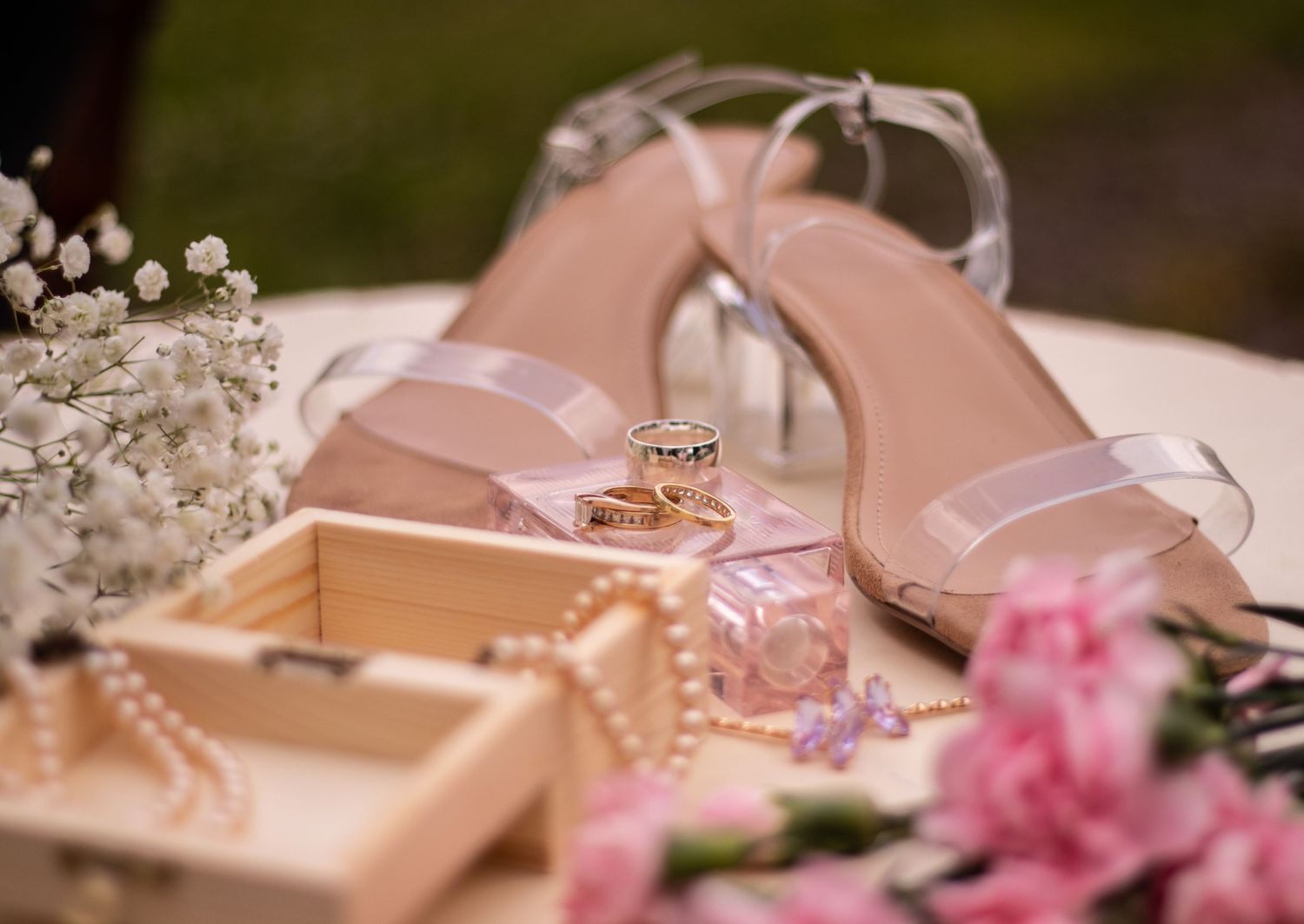 Wedding details with pink sandals, rings, and baby's breath flowers on blush background.