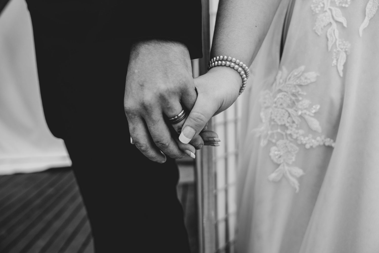 Close-up black and white photo of couple holding hands with lace dress detail.
