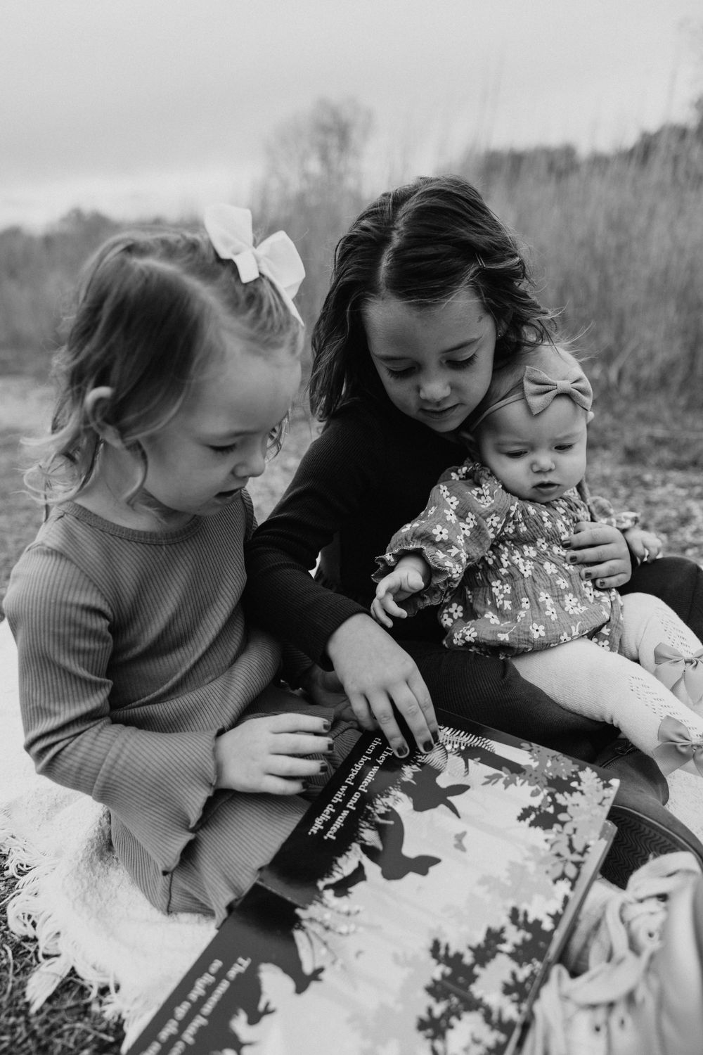 Black and white photo of children reading together outdoors on a blanket.